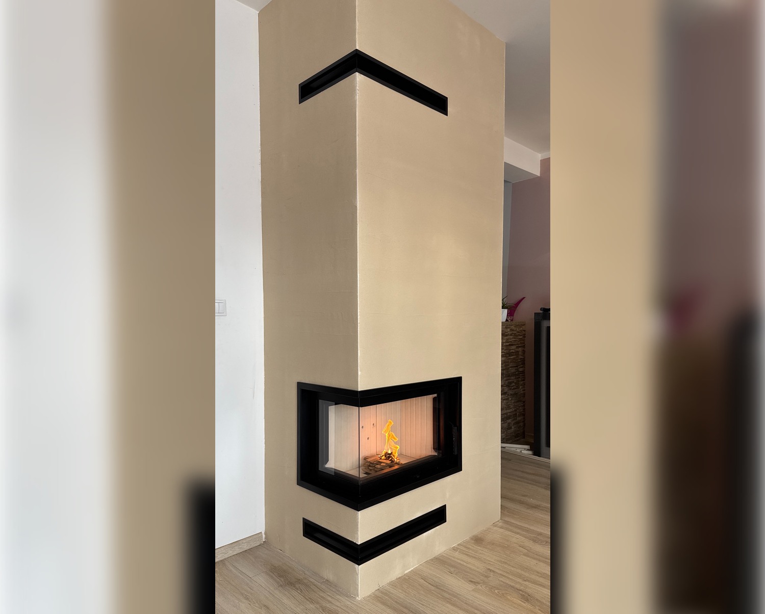 Narożny kominek z czarnymi detalami w beżowym wykończeniu, widoczny płomień. Realizacja z Oławy, nowoczesny design i minimalistyczny styl.