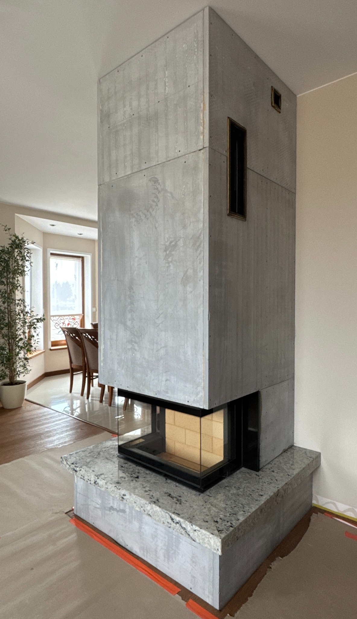 Nowoczesny kominek z betonu architektonicznego i kamiennym blatem, widoczny w salonie z elementami dekoracyjnymi. Minimalistyczny design.