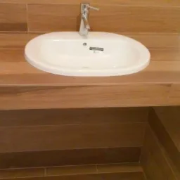 Umywalka wpuszczona w drewnopodobny blat z płytek, bateria chromowana, biała cegiełka na ścianie. Aranżacja łazienki z bliska.