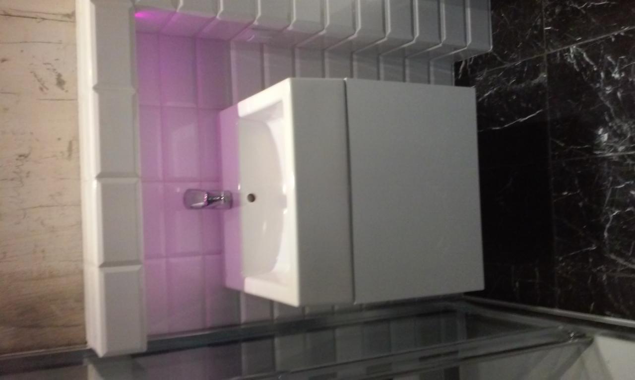 Nowoczesna, biała umywalka z szafką w łazience z podświetleniem LED i czarnymi marmurowymi płytkami. Minimalistyczny design.