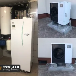 Kompaktowa, biała jednostka wewnętrzna pompy ciepła Ecodan w pomieszczeniu technicznym oraz dwie jednostki zewnętrzne Mitsubishi na betonowych podstawach przed budynkiem.