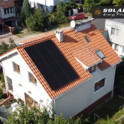 Widok z góry na dom jednorodzinny w Solcu Kujawskim z panelami słonecznymi na dachu z czerwonej dachówki, widoczny ogród i sąsiednie budynki.