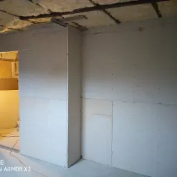 Montaż płyt kartonowo-gipsowych na ścianach i suficie z widoczną izolacją z wełny mineralnej, surowy stan przed szpachlowaniem i malowaniem.