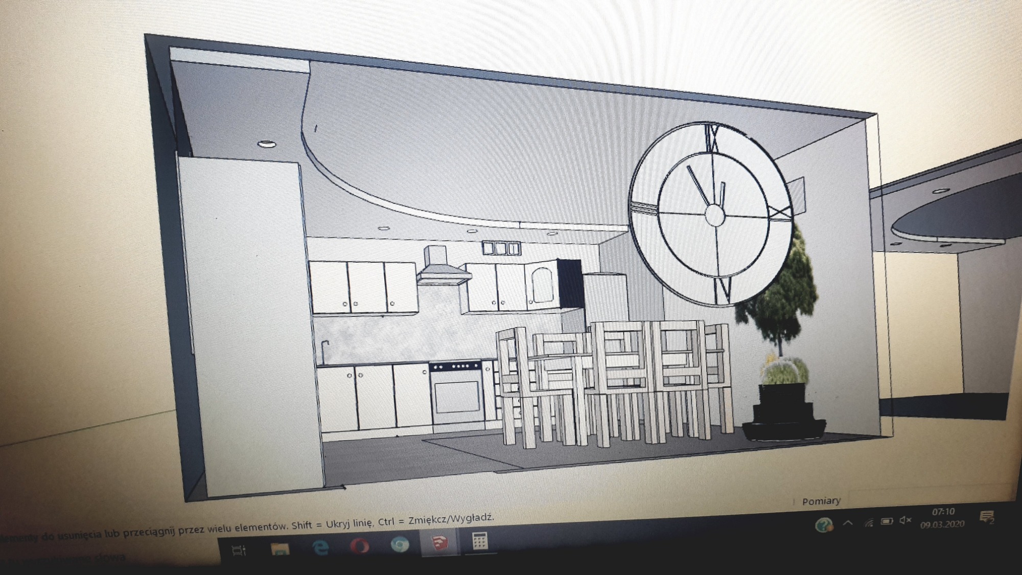 Wizualizacja 3D projektu wnętrza kuchni z jadalnią, prezentująca białe meble kuchenne, drewniany stół z krzesłami oraz duży zegar na ścianie. Widoczny fragment monitora laptopa z interfejsem...