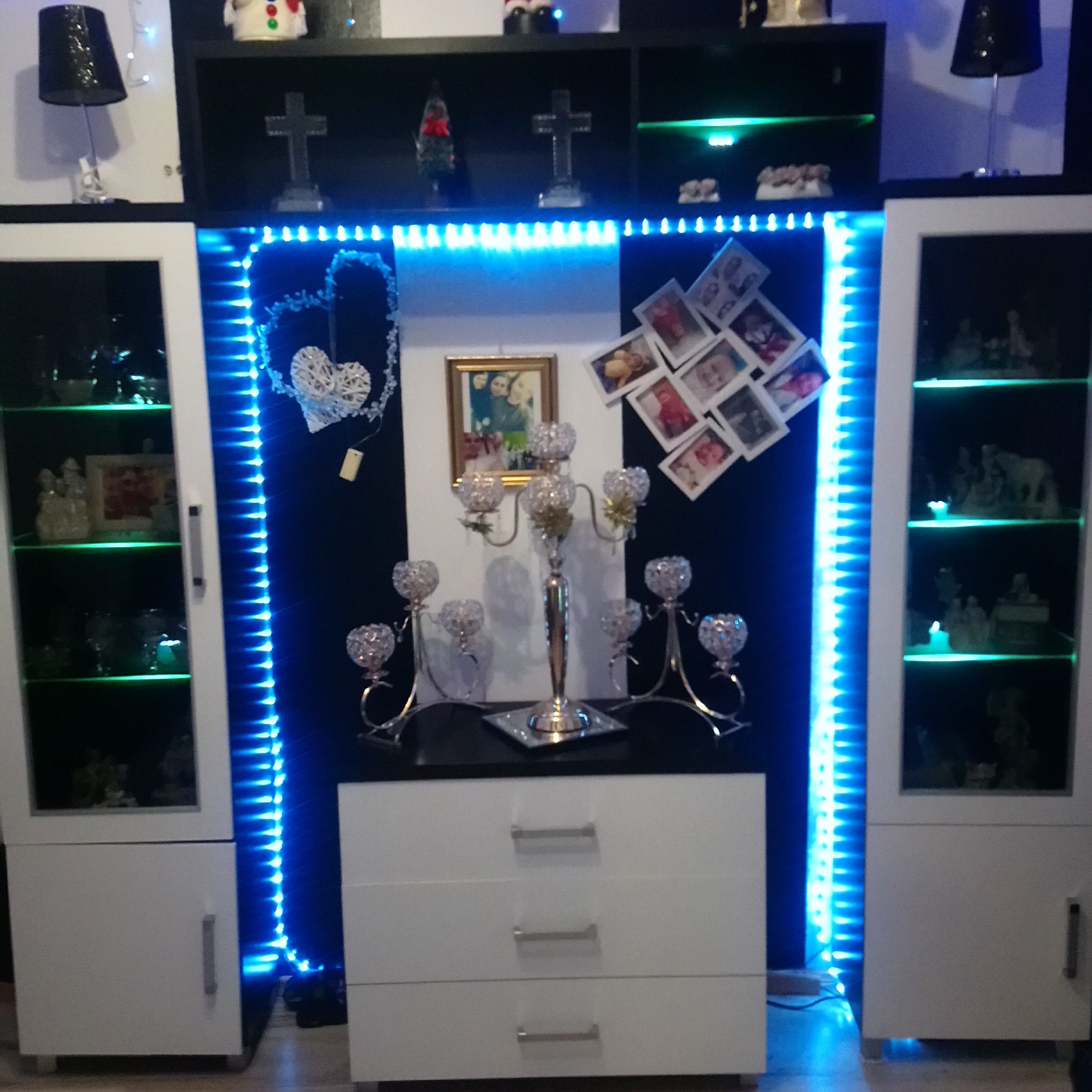 Zestaw mebli pokojowych z oświetleniem LED w Płocku: białe szafki z przeszkleniami, komoda z szufladami, półki z dekoracjami i zdjęciami.