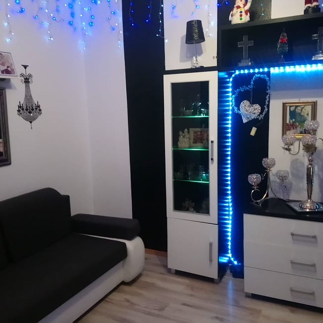 Nowoczesny salon z czarno-białymi meblami, oświetleniem LED w kolorze niebieskim i dekoracjami ściennymi, w tym kryształowym żyrandolem, ukazujący aranżację wnętrza.