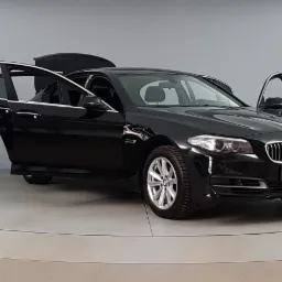 Czarny samochód BMW z otwartymi drzwiami i bagażnikiem, prezentowany w studiu na obrotowej platformie.