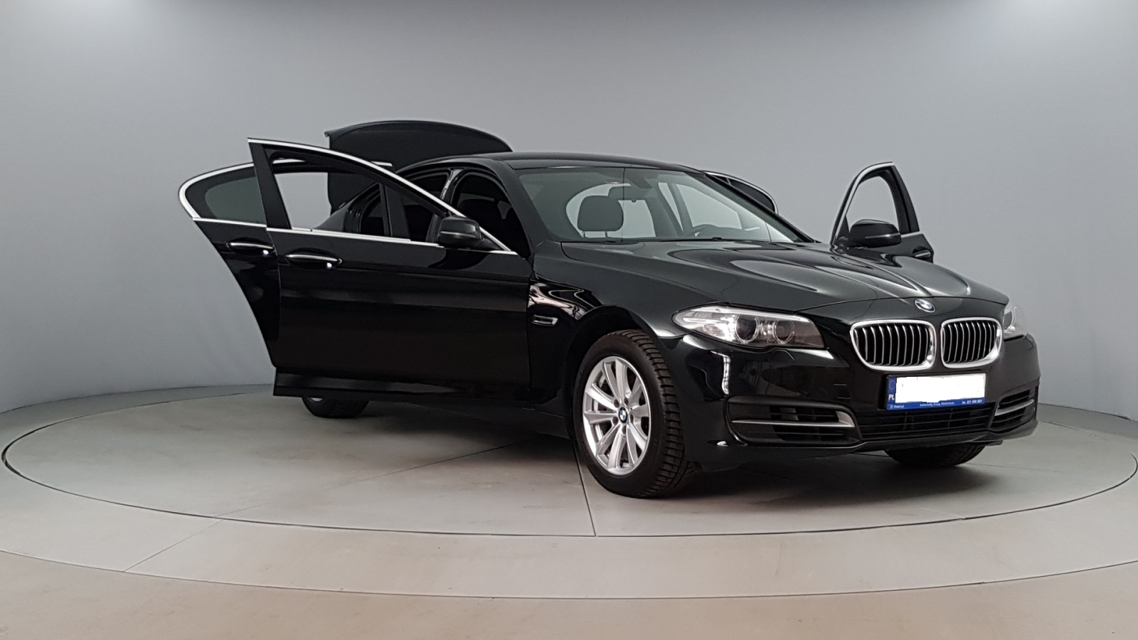 Czarny samochód BMW z otwartymi drzwiami i bagażnikiem, prezentowany w studiu na obrotowej platformie.