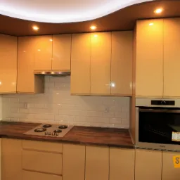 Beżowa zabudowa kuchenna z drewnianym blatem i białymi płytkami na ścianie, zrealizowana w Chełmie, z widoczną płytą grzewczą i piekarnikiem w zabudowie oraz półkami na wino.