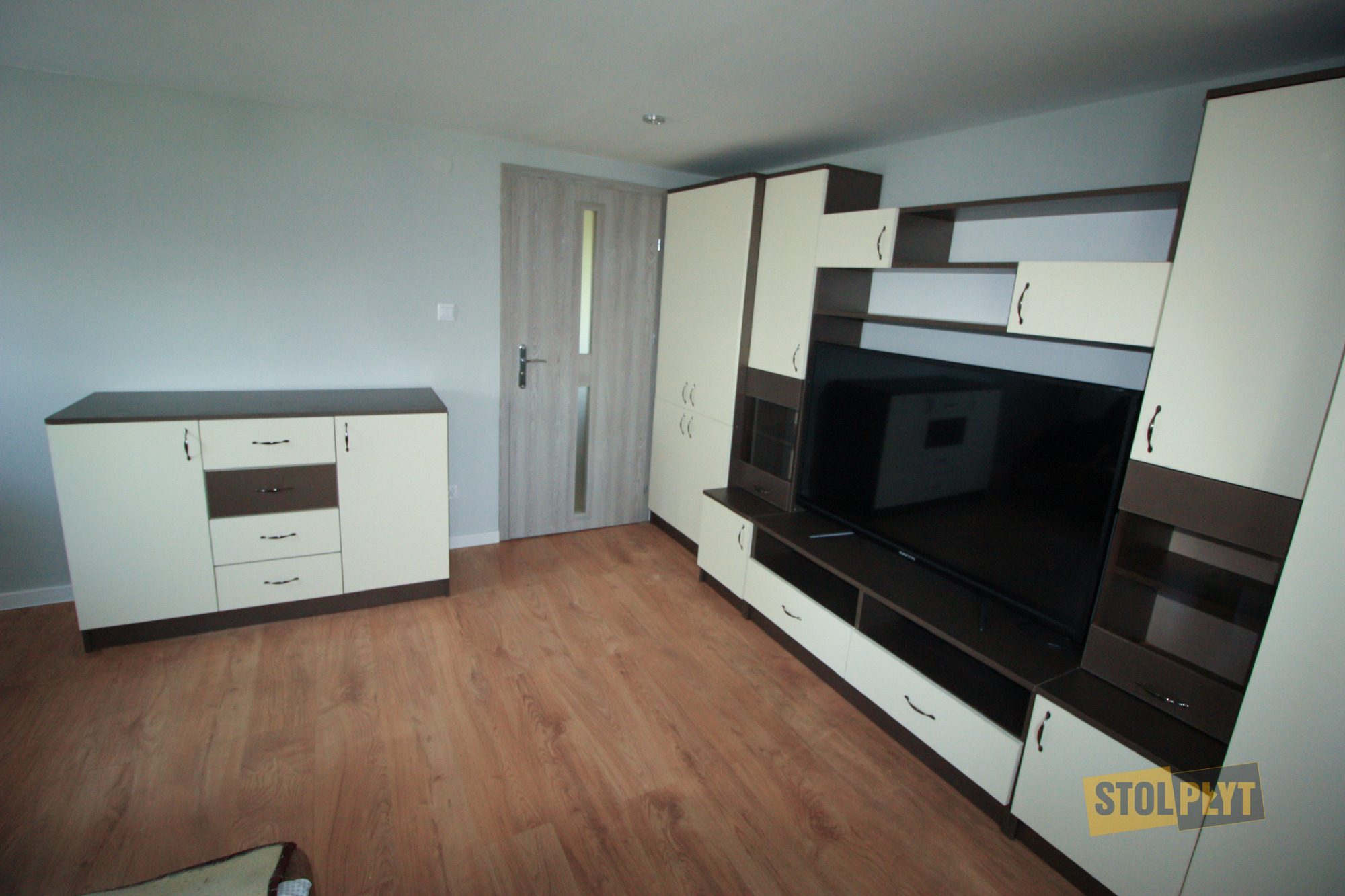 Nowoczesna zabudowa salonu z szafkami w kolorze kremowym i brązowym, z komodą i szafką RTV pod telewizor, na podłodze panele drewnopodobne.