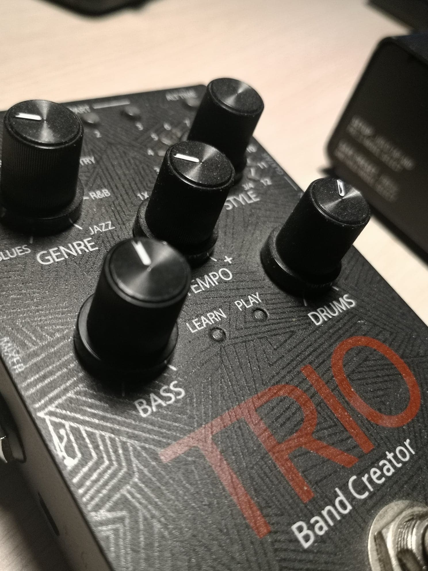 Czarny pedał gitarowy Trio Band Creator z widocznymi pokrętłami do ustawiania gatunku muzycznego, stylu, tempa i basu.