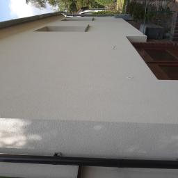 Majonez Buduje - Świeżo otynkowana, jasna elewacja budynku jednorodzinnego z widocznymi elementami drenażu i fragmentem muru z czerwonej cegły.