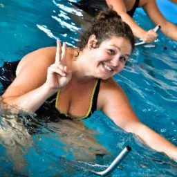 Uśmiechnięta kobieta w wodzie, wykonująca ćwiczenia na rowerze wodnym, pokazująca znak zwycięstwa