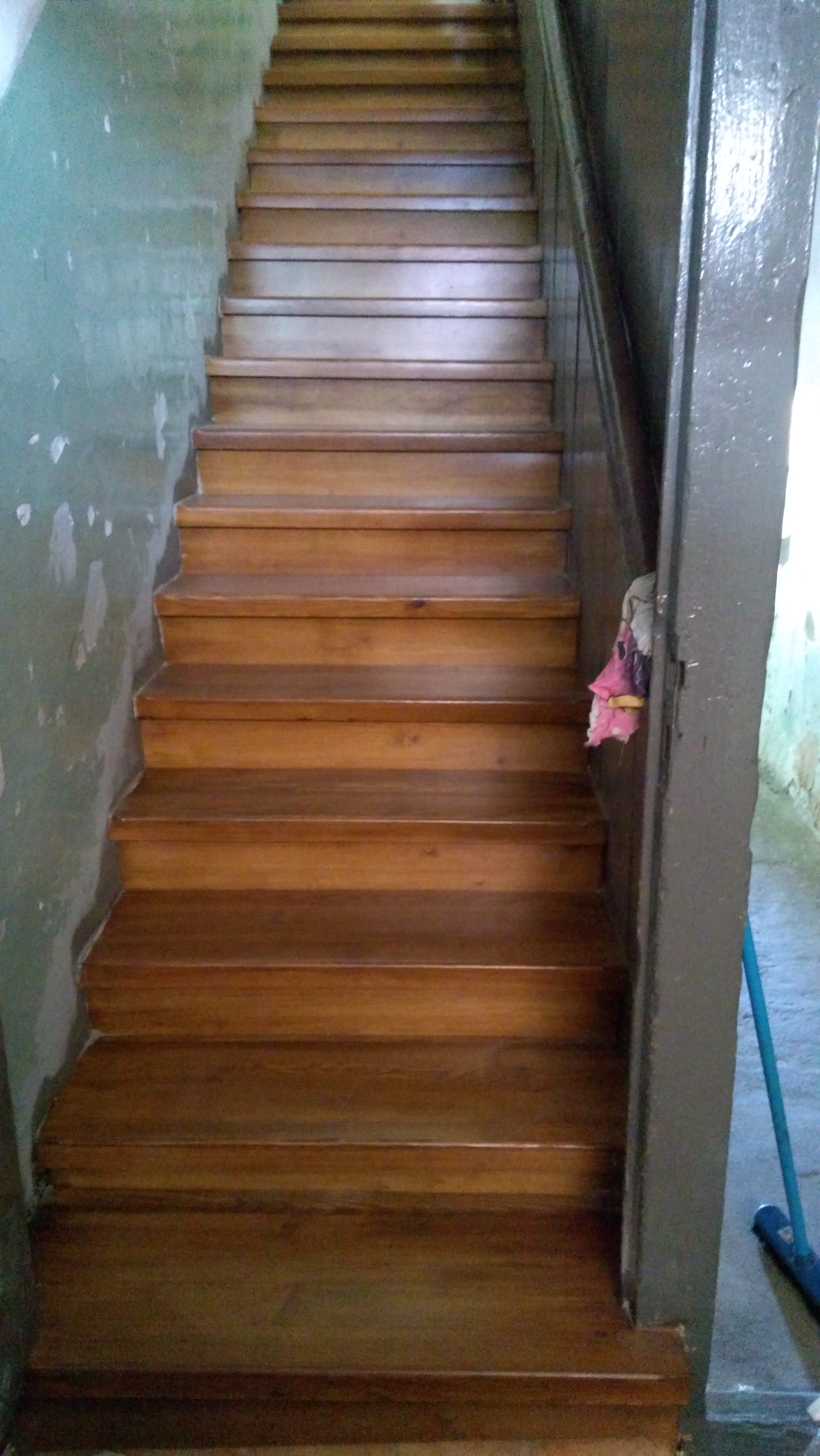 Drewniane schody w trakcie renowacji, widoczne ślady starej farby na ścianie i szpachli, oświetlenie dzienne, perspektywa od dołu.