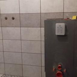 Krzysztof - Montaż stelaża podtynkowego WC z widocznymi rurami instalacyjnymi na tle częściowo wyłożonej płytkami ściany i podłogi w łazience.
