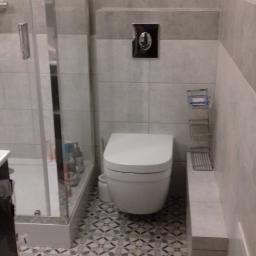 Krzysztof - Wykończona łazienka z kabiną prysznicową, podwieszaną toaletą, mozaikową podłogą i szarymi płytkami ściennymi z ciemniejszym pasem dekoracyjnym.