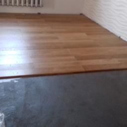 Krzysztof - Fragment pokoju z częściowo ułożonymi panelami podłogowymi w odcieniach brązu, widoczna podłoga przygotowana pod montaż i fragment ściany z dekoracyjną fakturą fal, w tle grzejnik.