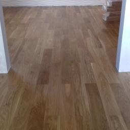 Krzysztof - Ułożone panele podłogowe o naturalnym odcieniu drewna, widoczne fragmenty ścian z dekoracyjną strukturą i paczka paneli w folii w tle.