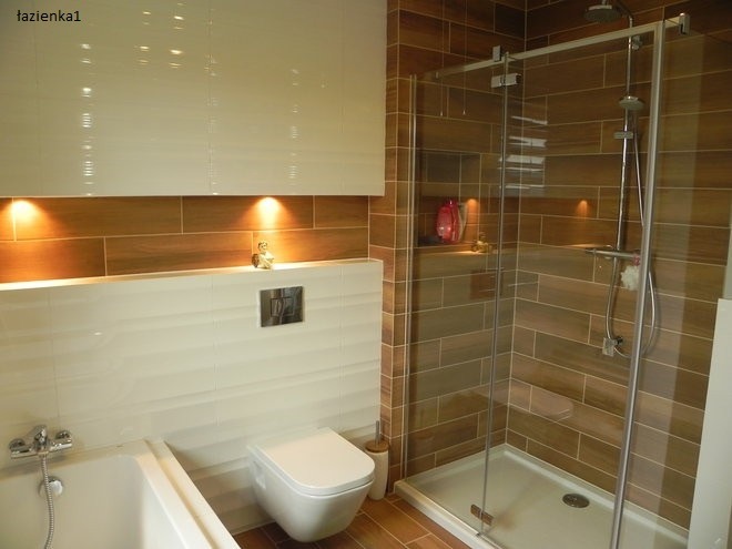 Nowoczesna łazienka z brązowymi płytkami imitującymi drewno, kabiną prysznicową typu walk-in, podwieszaną toaletą i białymi szafkami z oświetleniem punktowym.