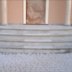 Wykończone, półokrągłe, kamienne schody wejściowe z kolumnami, prowadzące do drzwi zabezpieczonych folią. Ułożona kostka brukowa na podjeździe.