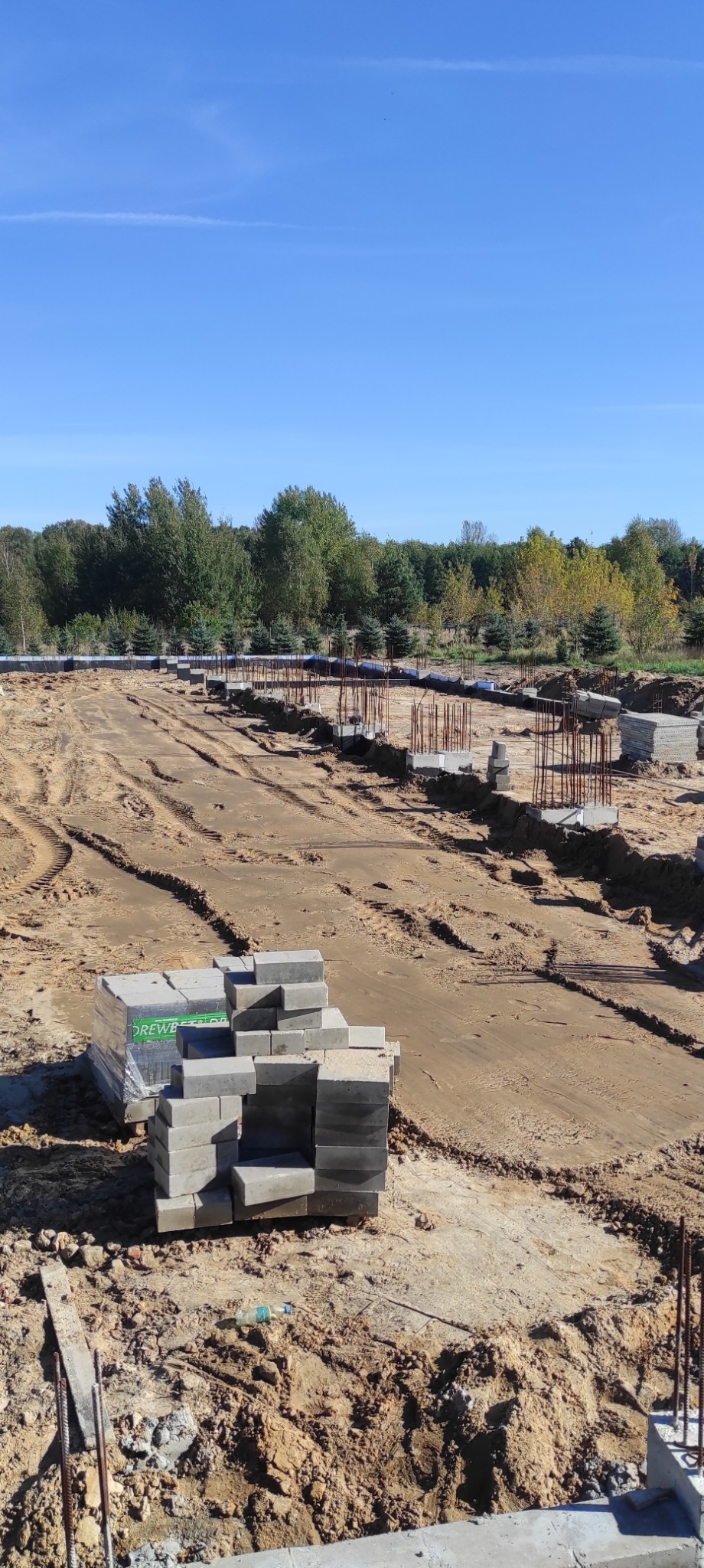 Fundamenty pod budynek w trakcie budowy, widoczne zbrojenia i bloczki betonowe na placu budowy w słoneczny dzień.