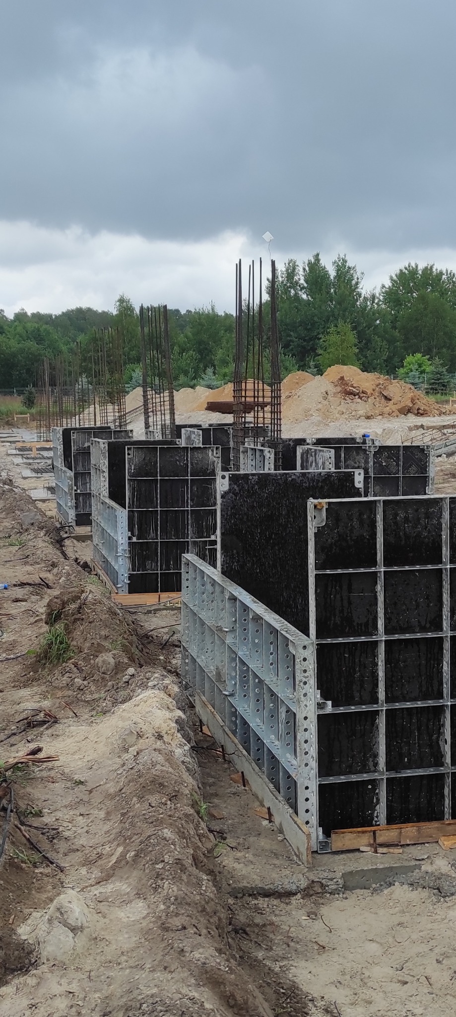 Przygotowanie szalunków i zbrojenia pod fundamenty budynku żelbetowego na placu budowy w pochmurny dzień.