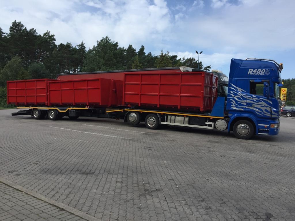 Niebieska ciężarówka Scania R480 z przyczepą niskopodwoziową przewożącą trzy czerwone kontenery, zaparkowana na brukowanym placu.