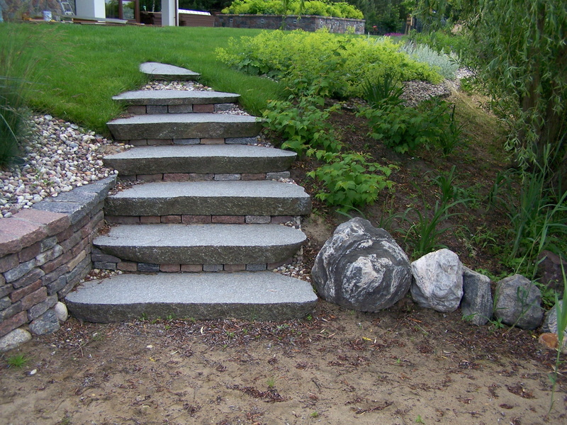 Stopnie z szarego kamienia prowadzące w górę zbocza, z murem oporowym po lewej stronie i dekoracyjnymi kamieniami po prawej.