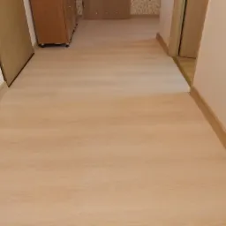 Jasna, drewnopodobna podłoga w korytarzu mieszkania w Zielonej Górze, z widocznymi listwami przypodłogowymi i fragmentami drzwi.