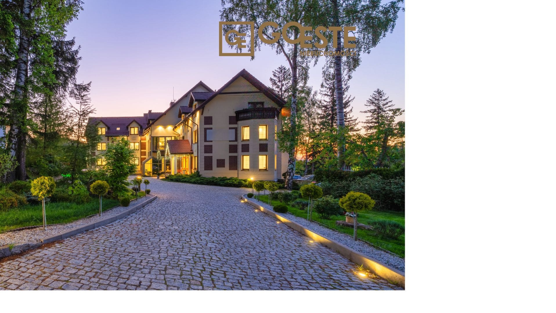 Elegancki, trzypiętrowy budynek z brązowymi akcentami, oświetlony ciepłym światłem o zmierzchu, z brukowaną drogą dojazdową i starannie utrzymanym ogrodem z kulistymi krzewami.