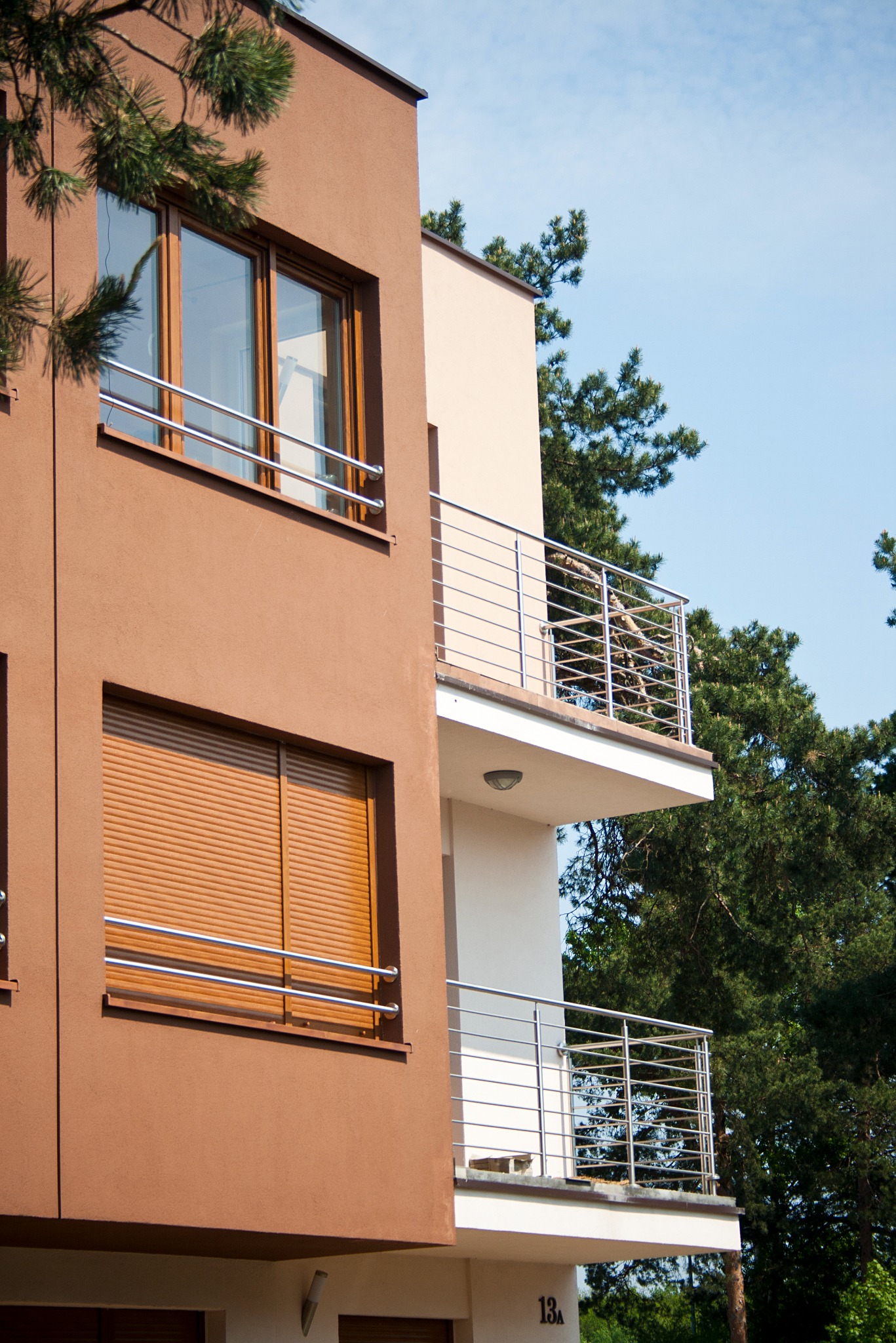 Dwupiętrowy budynek z balkonami i roletami zewnętrznymi, elewacja w odcieniach brązu i beżu, nowoczesna architektura.