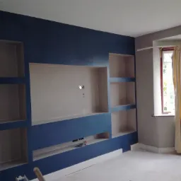 Ściana w pokoju po malowaniu z zabudową z płyt kartonowo-gipsowych, pomalowana na granatowo, z widocznymi otworami na kable w dolnej wnęce i gniazdko elektryczne w środkowej wnęce.