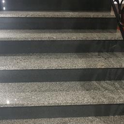 Zmaźlok - Granitowe schody z czarnymi podstopnicami, oświetlone punktowo, z dekoracyjną, kutą balustradą.