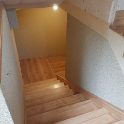 Zmaźlok - Drewniane schody prowadzące w dół, wykończone jasnym drewnem, z widocznym oświetleniem i teksturowanymi ścianami.