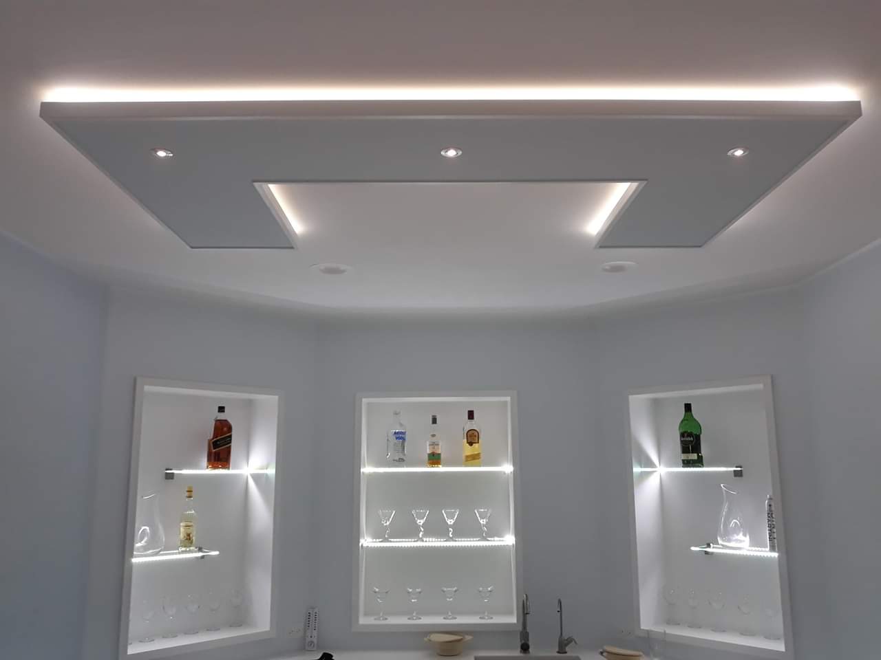 Nowoczesny barek wnękowy z podświetlanymi półkami i designerskim sufitem podwieszanym z oświetleniem punktowym i ledowym.