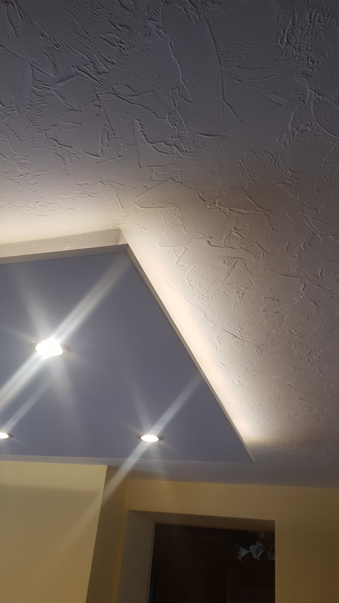 Wykończony sufit z oświetleniem punktowym i dekoracyjną strukturą, widok z dołu.