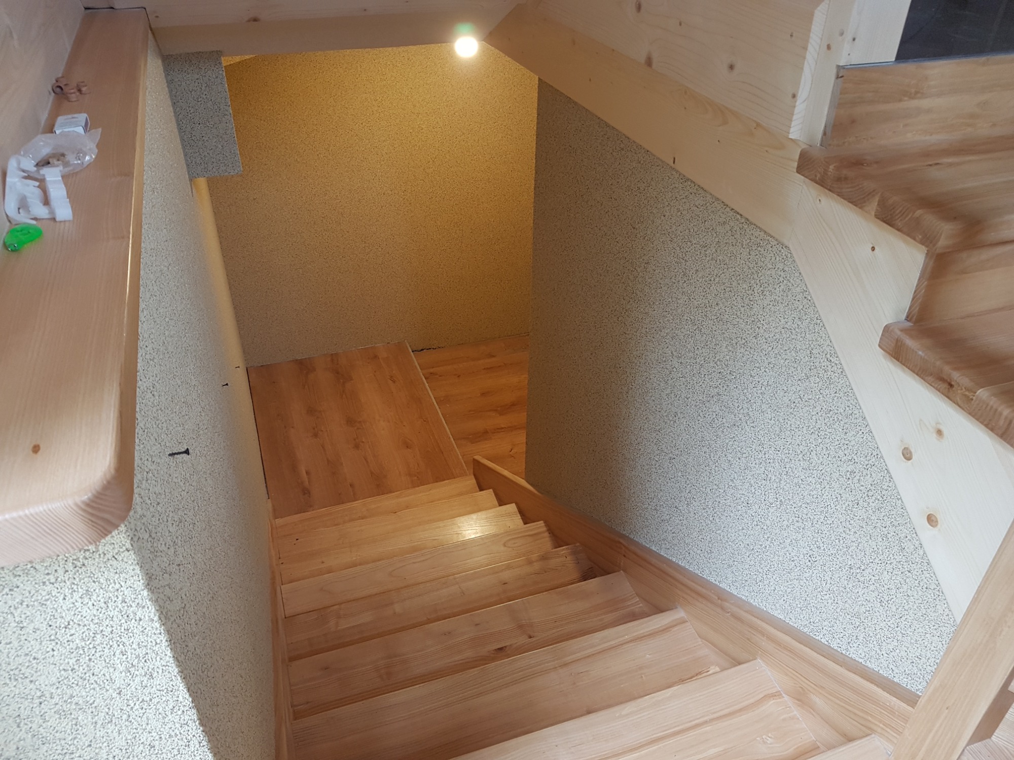 Drewniane schody prowadzące w dół, wykończone jasnym drewnem, z widocznym oświetleniem i teksturowanymi ścianami.