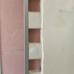 Konstrukcja ściany z profili metalowych i częściowo wypełniona izolacją, widoczne fragmenty białej ściany z zaznaczeniami ołówkiem.