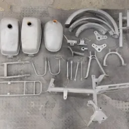 Elementy motocyklowe, w tym zbiorniki paliwa, błotniki i rama, po obróbce przygotowawczej, leżące na folii bąbelkowej.