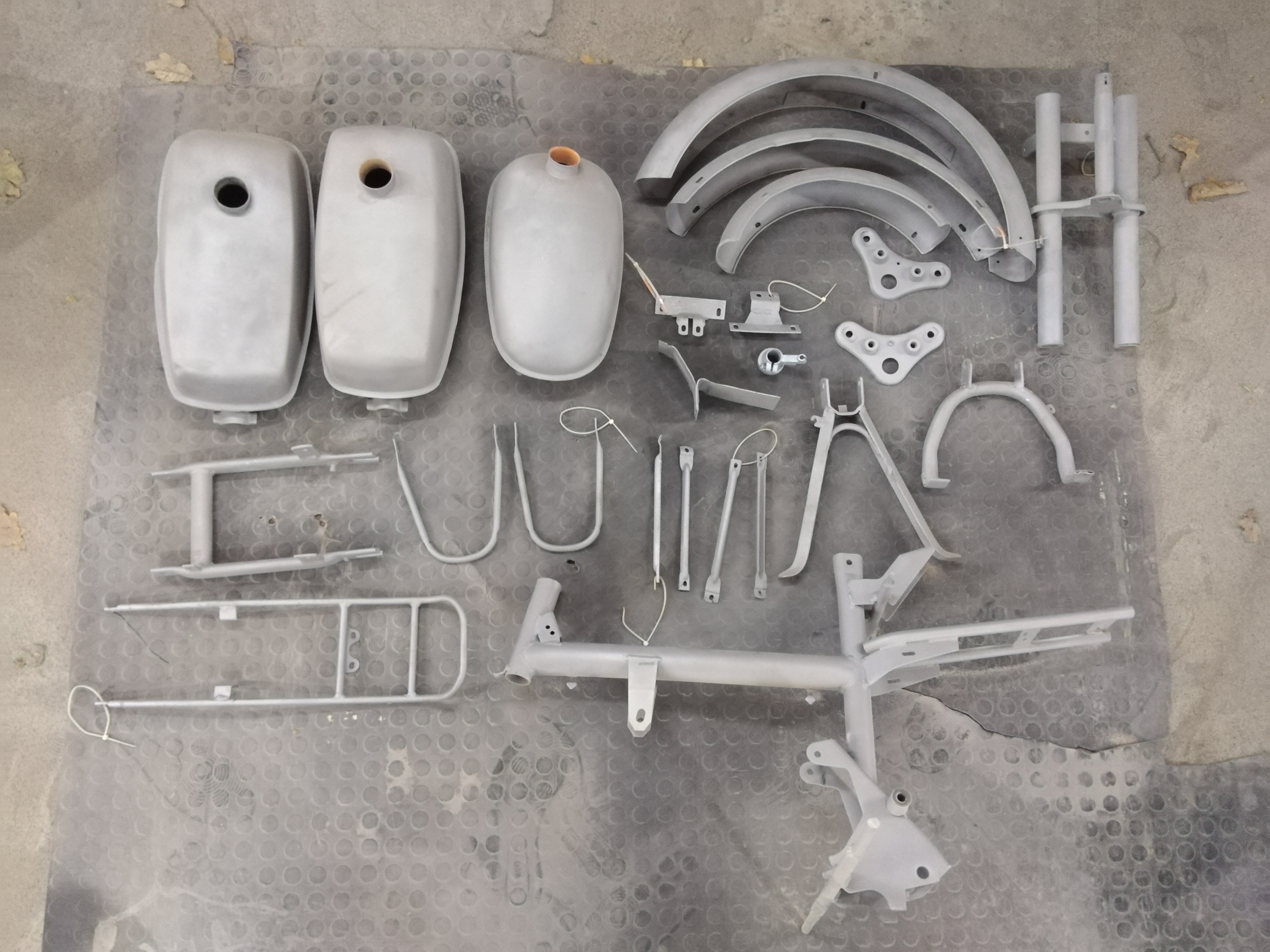 Elementy motocyklowe, w tym zbiorniki paliwa, błotniki i rama, po obróbce przygotowawczej, leżące na folii bąbelkowej.