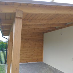 Robkalwik - Drewniana konstrukcja z belek i desek, prawdopodobnie zadaszenie tarasu lub wiata, z widoczną ścianą z desek i fragmentem posesji z zielenią w tle.