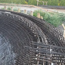 Siatka zbrojeniowa ułożona warstwowo na budowie, widoczne białe dystanse i drewniane elementy szalunku w tle.