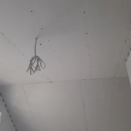 Montaż płyt na suficie podwieszanym, widoczne kable oświetleniowe zwisające z otworu, ślady po wkrętach mocujących.