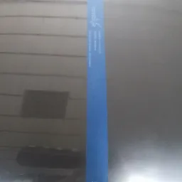 Ciemny element karoserii samochodu z widocznym odblaskiem światła po polerowaniu, z niebieskim paskiem taśmy maskującej z napisem 'matve' w pionie.