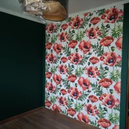 Pokój po remoncie: ściana z ciemnozieloną farbą kontrastuje z tapetą w czerwone maki, widoczna drewniana podłoga.