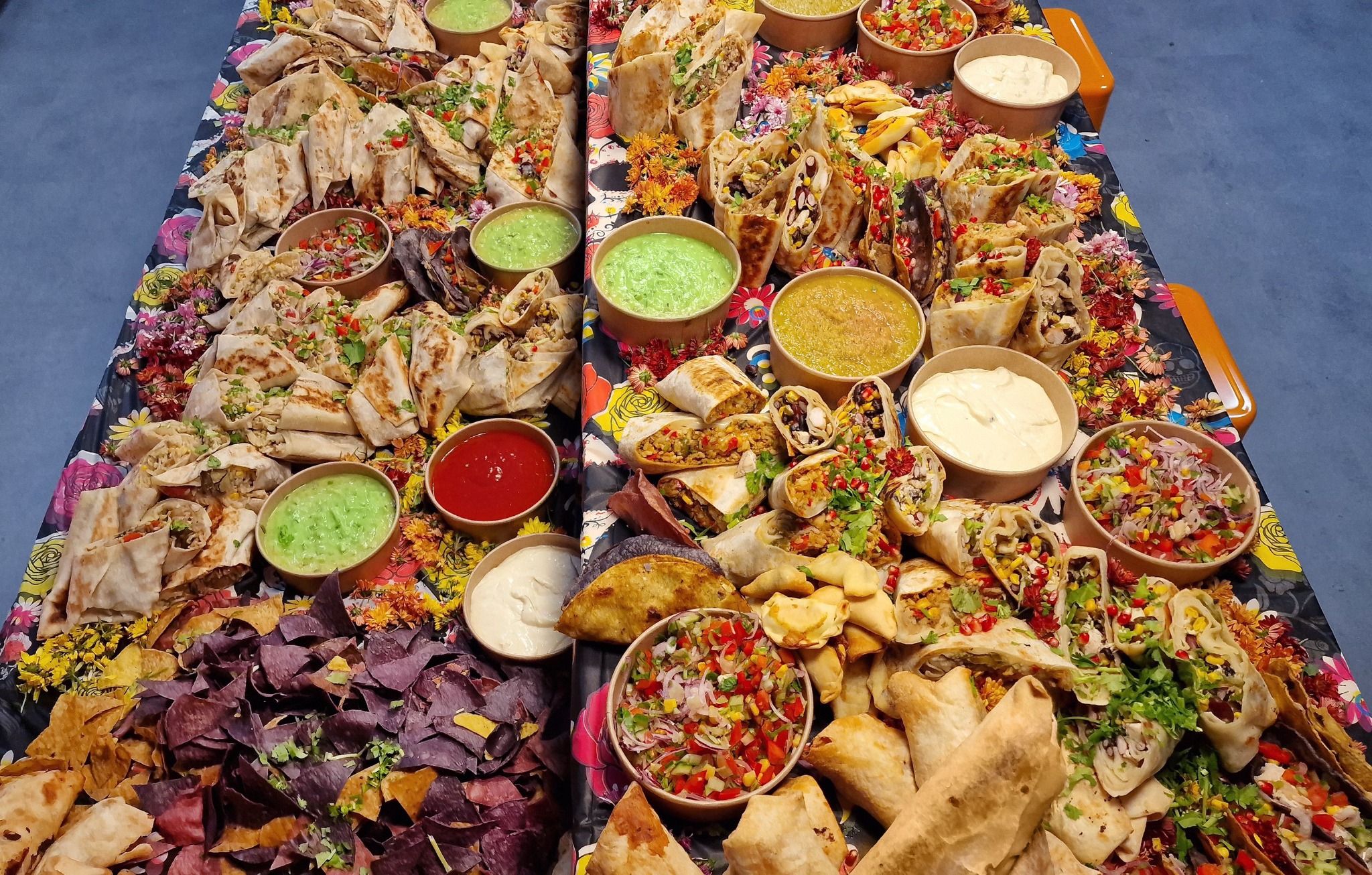 Rozbudowany catering meksykański: różnorodne tortille, quesadille, nachosy, salsy i dipy ułożone na stole z kwiatowym obrusem.