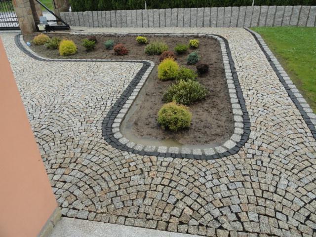 Wykończony podjazd z jasnej kostki, obrzeża z ciemnej kostki, tworzące rabatę z roślinami. Widok z góry, podkreślający wzór ułożenia kostki.