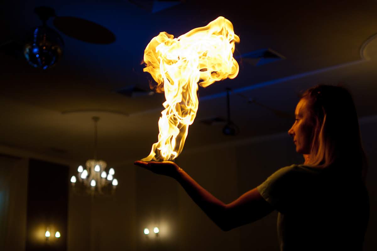 Kobieta w Grabinie prezentuje płomień unoszący się nad jej dłonią, w tle widoczny żyrandol i kula dyskotekowa.