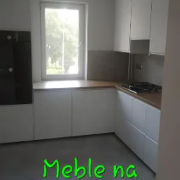 Nowoczesna, jasna kuchnia z białymi szafkami na wymiar i drewnianym blatem, widok z niskiego kąta, szara podłoga z połyskiem.