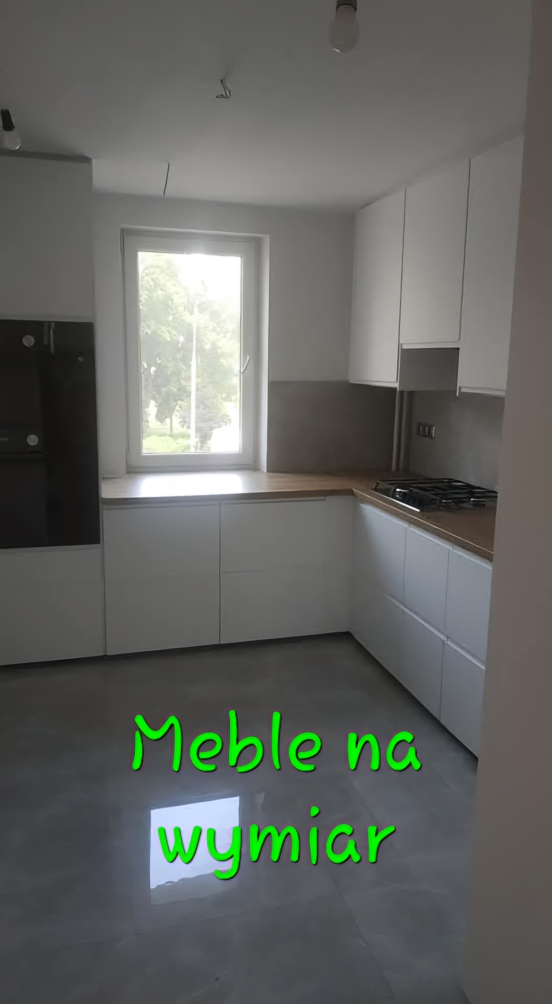 Nowoczesna, jasna kuchnia z białymi szafkami na wymiar i drewnianym blatem, widok z niskiego kąta, szara podłoga z połyskiem.